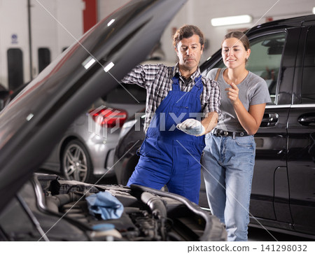 Mechanic consults woman on repairs under hood of car Mechanic consults woman on repairs under hood of car 141298032