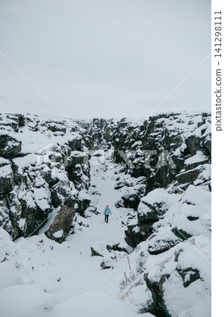 Person hiking through a snowy gorge in Thingvellir National Park, Iceland. 141298111