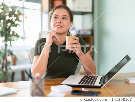 Young woman sitting at office desk drinking coffee 141298167