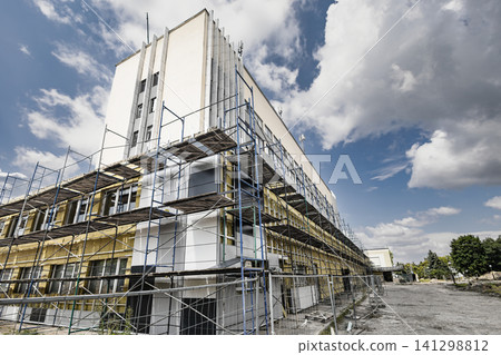 Workers are applying mineral wool insulation to an industrial building as part of a reconstruction project. Scaffolding surrounds the structure for access Workers are applying mineral wool insulation to an industrial building as part of a reconstruction project. Scaffolding surrounds the structure for access 141298812
