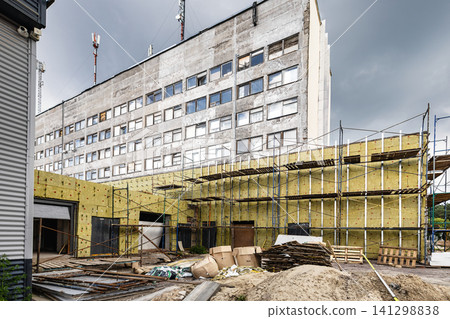 Workers are applying mineral wool insulation to the exterior of an office building. Scaffolding surrounds the structure as reconstruction takes place Workers are applying mineral wool insulation to the exterior of an office building. Scaffolding surrounds the structure as reconstruction takes place 141298838