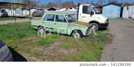 Old green sedan and white van parked in residential parking lot. 141299198