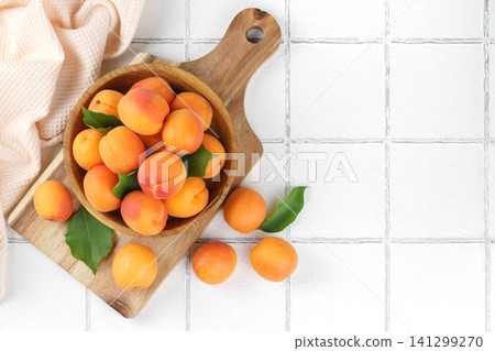 Fresh ripe apricots fruits in wooden bowl on cutting board over white tile background, copy space Fresh ripe apricots fruits in wooden bowl on cutting board over white tile background, copy space 141299270