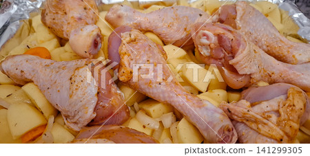 Raw chicken drumsticks and potatoes in baking tray. Raw chicken drumsticks and potatoes in baking tray. 141299305