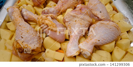 Raw chicken drumsticks and potatoes in baking tray. Raw chicken drumsticks and potatoes in baking tray. 141299306