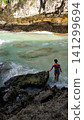 A slender woman in a swimsuit enjoys the turquoise ocean. Waves are crashing on the rocks. 141299694