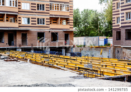 Construction site with yellow steel beams and brick apartment building under development Construction site with yellow steel beams and brick apartment building under development 141299785