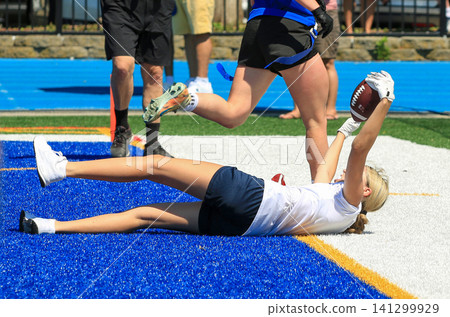 Girl Catches Football While Lying on the Field for a Touchdown in a flag football game Girl Catches Football While Lying on the Field for a Touchdown in a flag football game 141299929