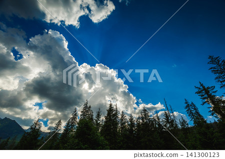 Dramatic blue sky with sun rays shining through fluffy white clouds 141300123