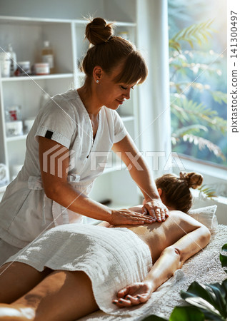 Natural Light Spa Back Massage Mature Female Therapist Presses Both Hands on Clients Upper Back on White Table With Sunlit Garden Window and Green Natural Light Spa Back Massage Mature Female Therapist Presses Both Hands on Clients Upper Back on White Table With Sunlit Garden Window and Green 141300497