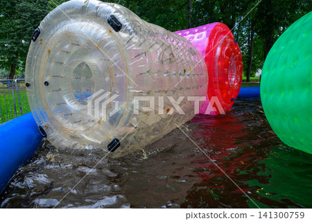 Transparent inflatable zimmerman rolls roll through shallow water 141300759