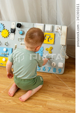 Child playing with zippers, switches and wheels on busyboard. Small hand movements strengthen muscles. Early education through sensory play. Discovering physical world Child playing with zippers, switches and wheels on busyboard. Small hand movements strengthen muscles. Early education through sensory play. Discovering physical world 141301011
