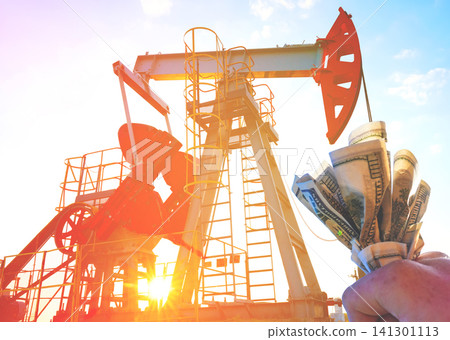 Men hold dollars near oil rig at sunset in industrial setup visible. Hand holding American dollars Men hold dollars near oil rig at sunset in industrial setup visible. Hand holding American dollars 141301113