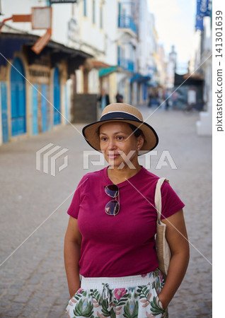Woman wearing straw hat and sunglasses in Essaouira old medina street, relaxed travel portrait Woman wearing straw hat and sunglasses in Essaouira old medina street, relaxed travel portrait 141301639