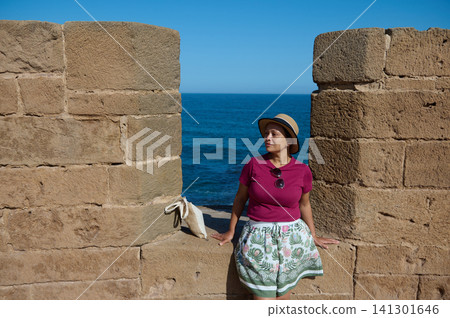 Woman relaxing on ancient ramparts overlooking the Atlantic in Essaouira old medina 141301646