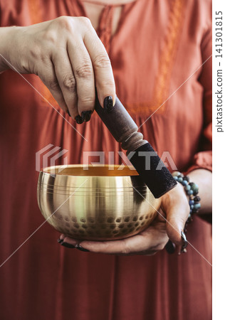 Woman playing a Tibetan singing bowl with a wooden mallet during a sound healing meditation session. Woman playing a Tibetan singing bowl with a wooden mallet during a sound healing meditation session. 141301815