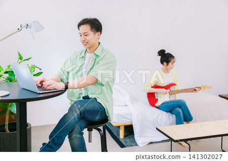 一個男人在工作,一個女人在彈吉他(這是她的業餘愛好)。 一個男人在工作,一個女人在彈吉他(這是她的業餘愛好)。 141302027