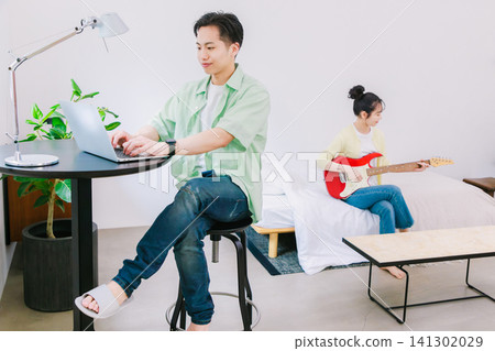 一個男人在工作,一個女人在彈吉他(這是她的業餘愛好)。 一個男人在工作,一個女人在彈吉他(這是她的業餘愛好)。 141302029