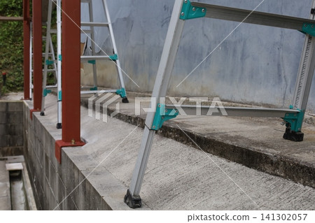建築工地,有鋁製梯子和放置在混凝土基座上的紅色鋼柱。 建築工地,有鋁製梯子和放置在混凝土基座上的紅色鋼柱。 141302057