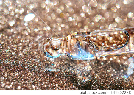 Cosmetic serum dropper dispensing liquid on glitter background Cosmetic serum dropper dispensing liquid on glitter background 141302288