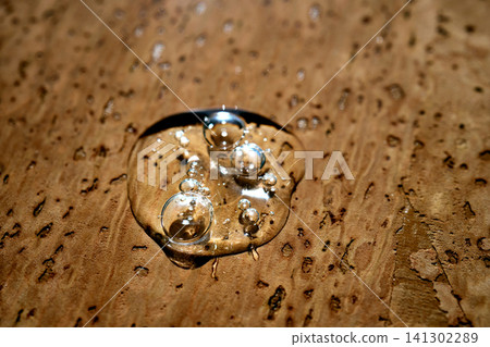 Clear cosmetic serum drop on textured cork surface Clear cosmetic serum drop on textured cork surface 141302289