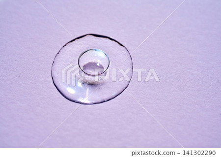 Clear cosmetic serum drop on purple background surface Clear cosmetic serum drop on purple background surface 141302290