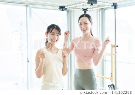 Pilates studio instructor and student strike a triumphant pose. Pilates studio instructor and student strike a triumphant pose. 141302298