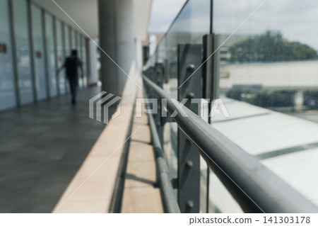 Perspective view of metal railings and glass fences in a building corridor (with blurred figures in the background). Perspective view of metal railings and glass fences in a building corridor (with blurred figures in the background). 141303178