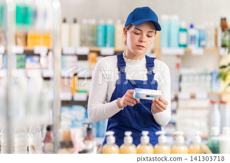 In sales area of pharmacy, builder woman examines packaging of gel for burns 141303718