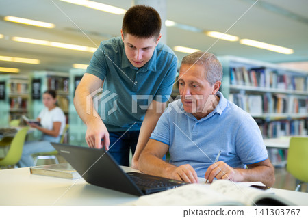 Young guy helping older man in laptop interface in library Young guy helping older man in laptop interface in library 141303767
