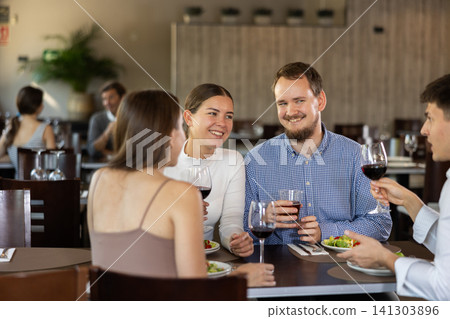Two couples meet for dinner at restaurant. They chat and drink wine Two couples meet for dinner at restaurant. They chat and drink wine 141303896