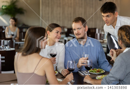 Helpful young waiter taking order from two couples in restaurant Helpful young waiter taking order from two couples in restaurant 141303898