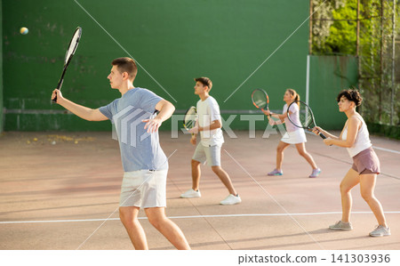 Young frontenis player swinging racquet to hit ball on outdoor court Young frontenis player swinging racquet to hit ball on outdoor court 141303936