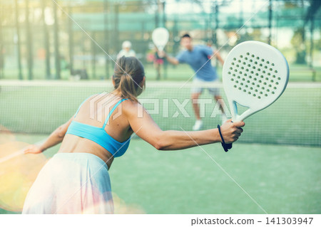 Sportive slim woman with racquet playing padel in court. View from back 141303947