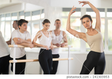 Pretty female choreographer conducting classes in ballet studio shows group correct performance of choreographic exercise Pretty female choreographer conducting classes in ballet studio shows group correct performance of choreographic exercise 141303953