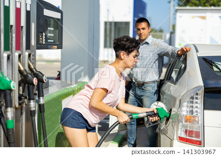 Latin woman filling up tank of her car with gasoline in gas station Latin woman filling up tank of her car with gasoline in gas station 141303967