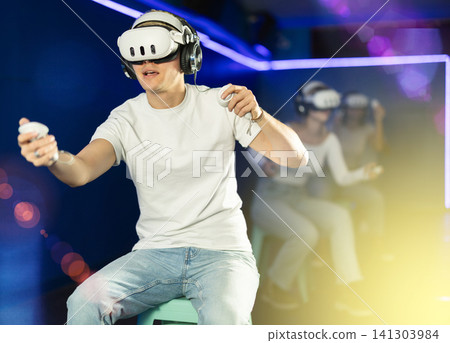 Guy playing game in virtual reality glasses in front of friends Guy playing game in virtual reality glasses in front of friends 141303984