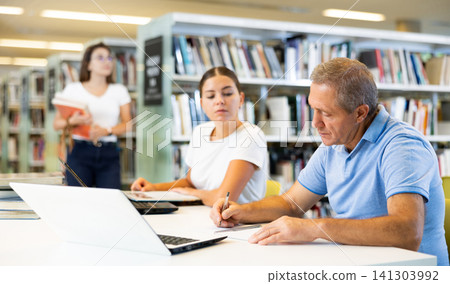Man and woman in casual clothes searching in Internet and writing in planner in the book space library Man and woman in casual clothes searching in Internet and writing in planner in the book space library 141303992