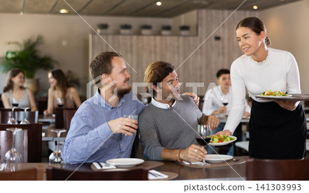 Waitress brings plates of salad for two friends in restaurant interior Waitress brings plates of salad for two friends in restaurant interior 141303993