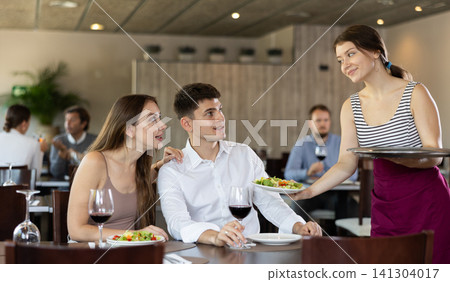 Waitress brings order to young man and woman couple Waitress brings order to young man and woman couple 141304017