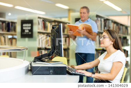 Positive Latin young woman typing on keyboard and searching info in Internet on a stationary computer in the library Positive Latin young woman typing on keyboard and searching info in Internet on a stationary computer in the library 141304029