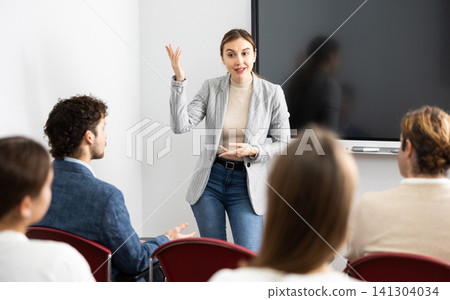 Portrait of young businesswoman standing near interactive board and participating in corporate seminar in auditorium Portrait of young businesswoman standing near interactive board and participating in corporate seminar in auditorium 141304034