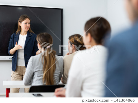 Positive successful woman near interactive board conducting business training for audience in classroom Positive successful woman near interactive board conducting business training for audience in classroom 141304066