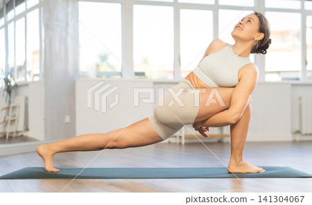 Young attractive smiling woman practicing yoga, doing revolved side angle pose in yoga gym Young attractive smiling woman practicing yoga, doing revolved side angle pose in yoga gym 141304067