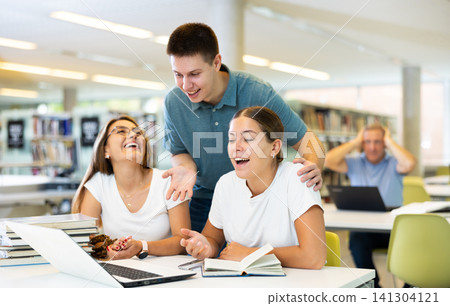 Young man in casual clothes explaining info to young women poiting on the screen of computer in the library Young man in casual clothes explaining info to young women poiting on the screen of computer in the library 141304121