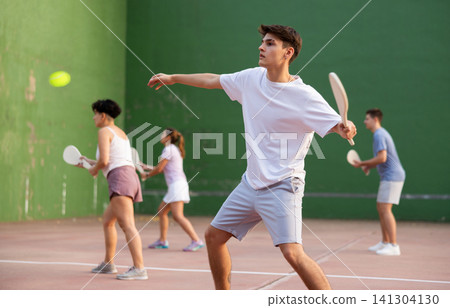 Concentrated young man paleta fronton player hitting ball with racket Concentrated young man paleta fronton player hitting ball with racket 141304130