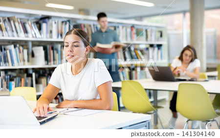 Portrait of woman studying at library using books and laptop 141304140