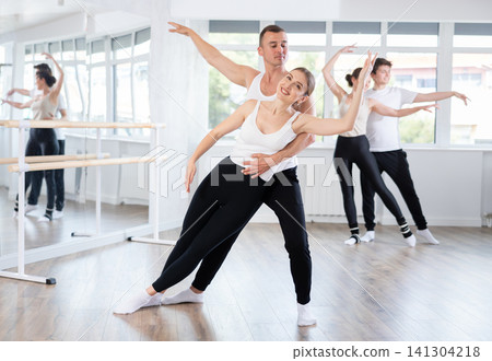 Happy ballet dancers couple performing choreography with support during group training classes in dance studio Happy ballet dancers couple performing choreography with support during group training classes in dance studio 141304218