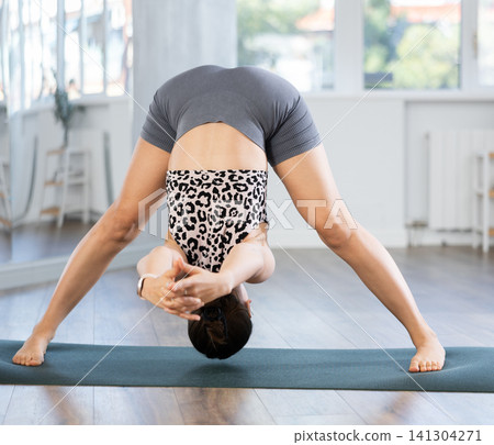 Sporty young woman performing advanced yoga posture in studio Sporty young woman performing advanced yoga posture in studio 141304271