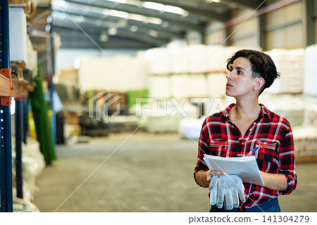 Female storekeeper checks availability of goods with documents in the building materials warehouse Female storekeeper checks availability of goods with documents in the building materials warehouse 141304279